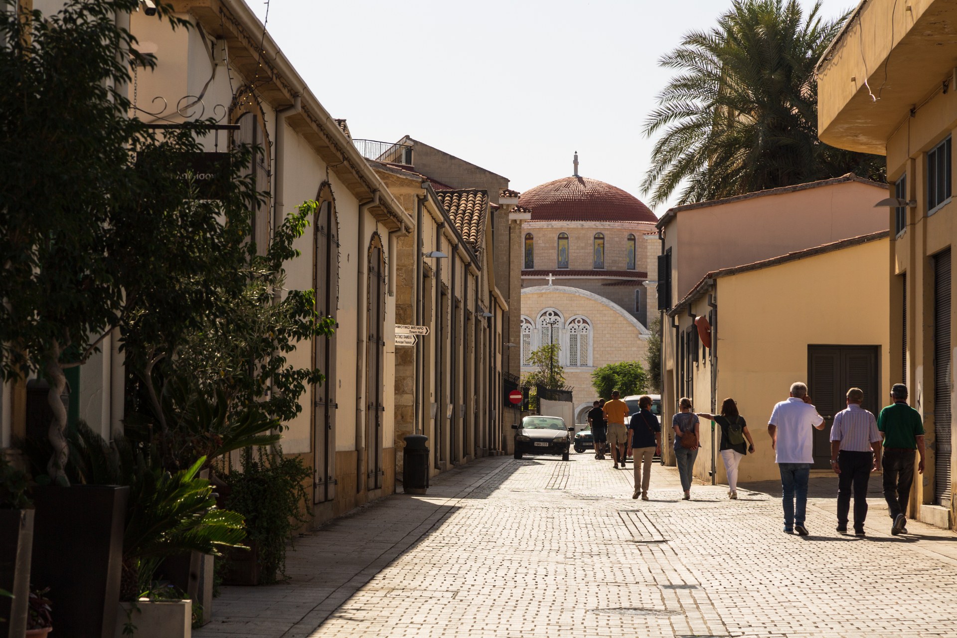 Pessoas a caminhar por uma rua estreita do centro histórico de Nicósia, em direção a uma catedral com cúpula
